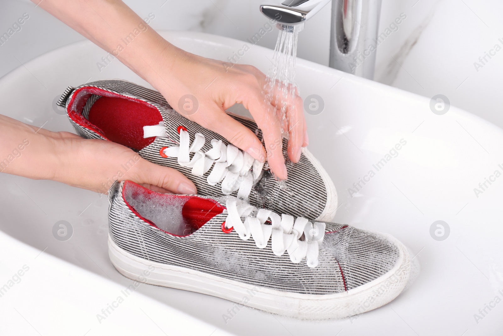 Photo of Woman washing sport shoe in sink, closeup