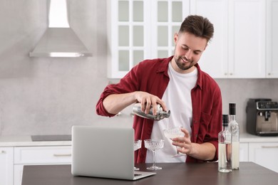 Photo of Man learning to make cocktail with online video on laptop at table in kitchen. Time for hobby