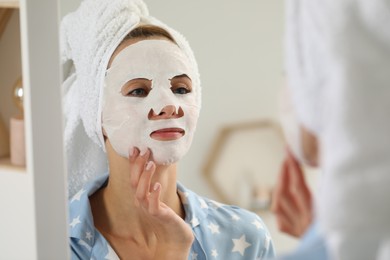 Photo of Young woman with face mask looking into mirror indoors. Spa treatments