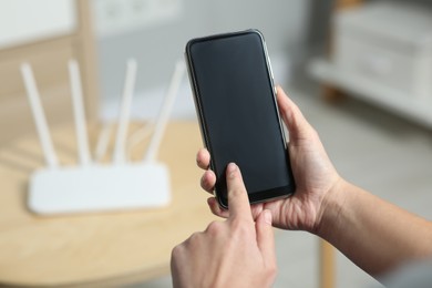 Photo of Woman with smartphone connecting to internet via Wi-Fi router indoors, closeup