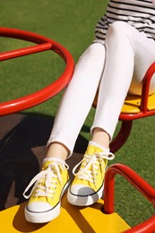 Photo of Woman in yellow classic old school sneakers on carousel outdoors, closeup