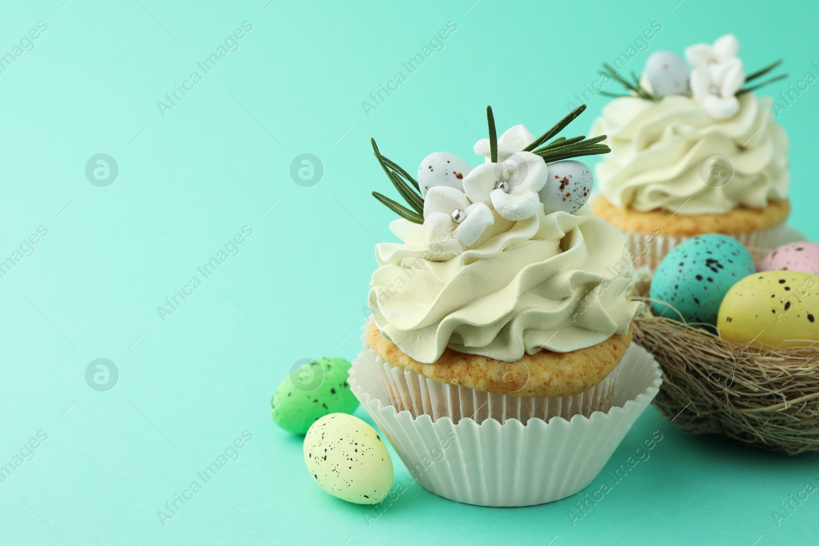 Photo of Tasty Easter cupcakes with vanilla cream and festive decor on turquoise background, space for text