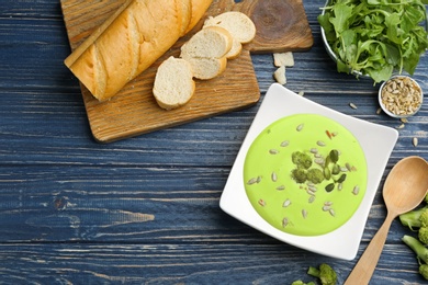 Photo of Flat lay composition with bowl of broccoli cream soup on blue wooden table. Space for text