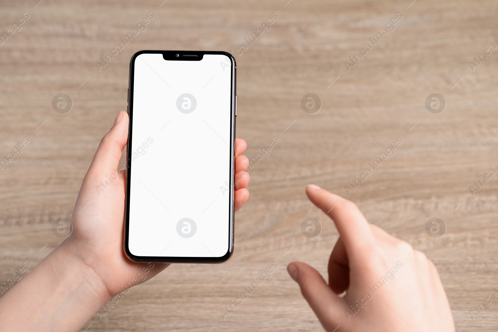 Photo of Woman holding smartphone with blank screen at wooden table, top view. Mockup for design