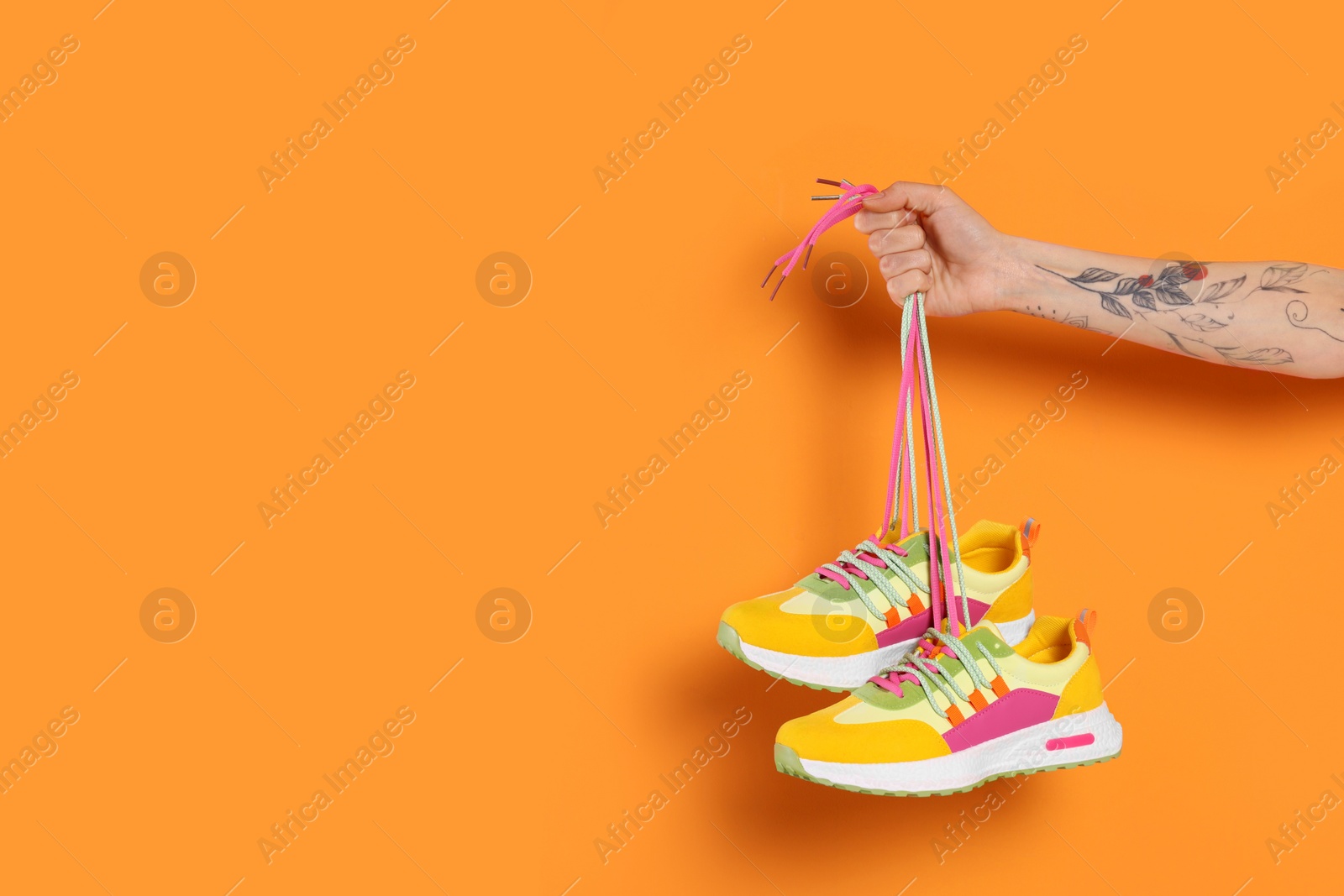 Photo of Woman holding pair of stylish colorful sneakers on orange background, closeup. Space for text