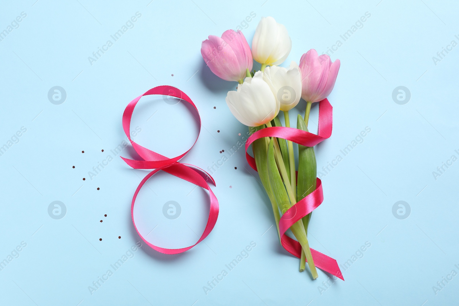 Photo of 8th of March greeting card design with pink ribbon and beautiful flowers on light blue background, flat lay. International Women's day