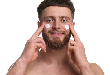 Handsome man applying moisturizing cream onto his face on white background