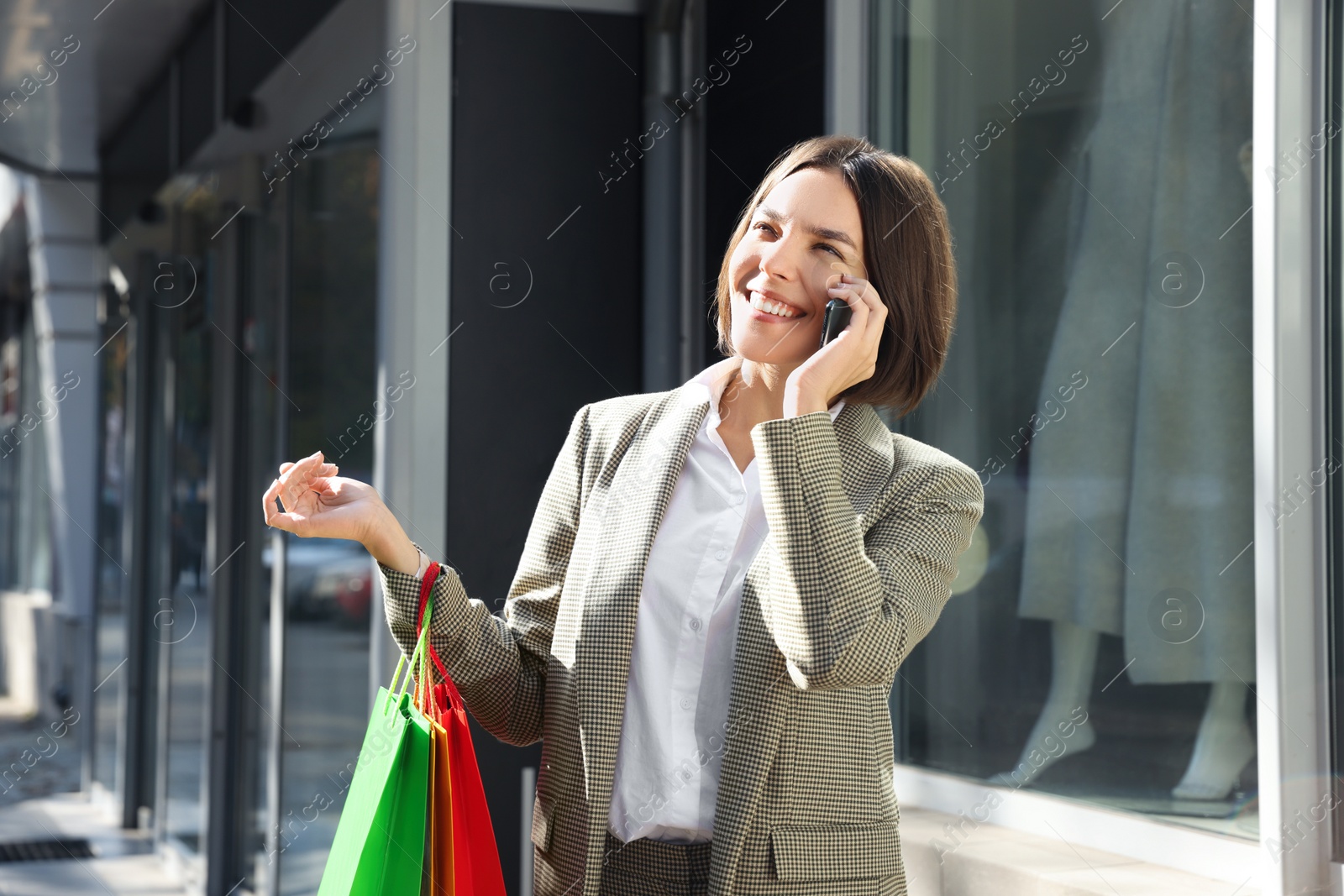 Photo of Special Promotion. Happy young woman with shopping bags and smartphone on city street