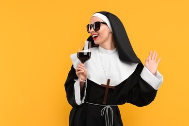 Photo of Happy woman in nun habit and sunglasses holding glass of wine against orange background. Space for text