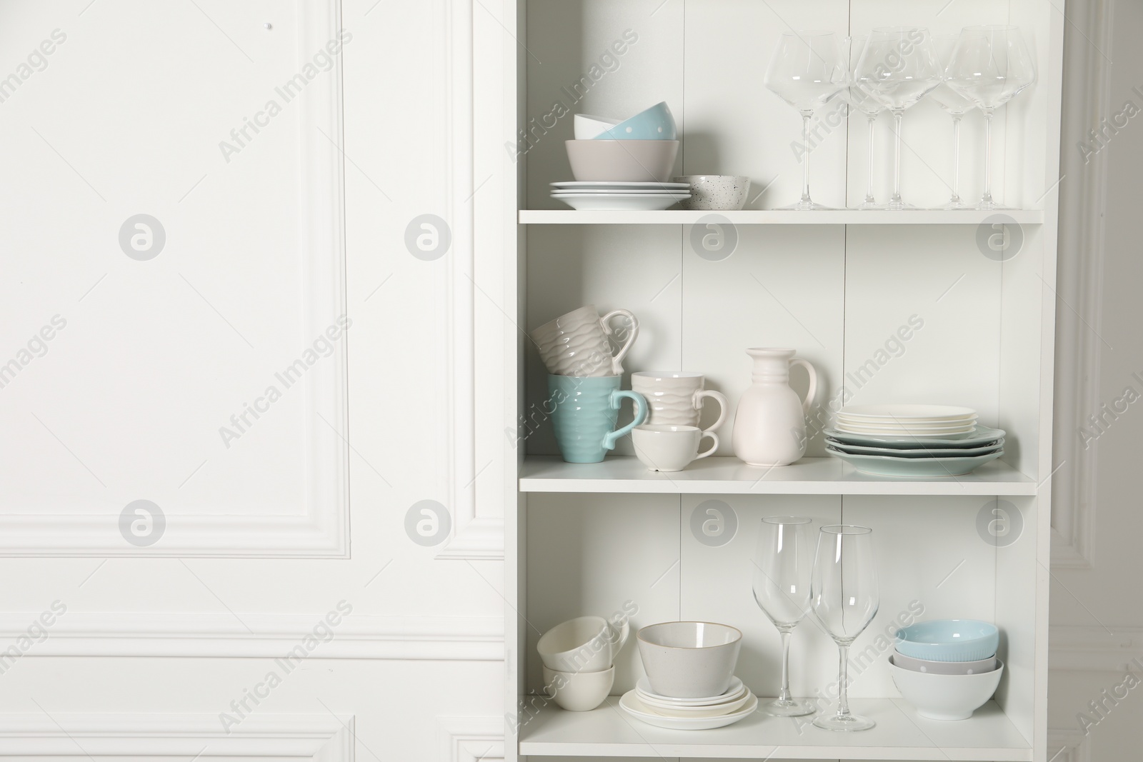 Photo of Different clean dishware and glasses on shelves in cabinet indoors