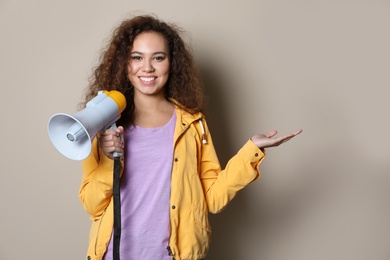 Young African-American woman with megaphone on color background. Space for text