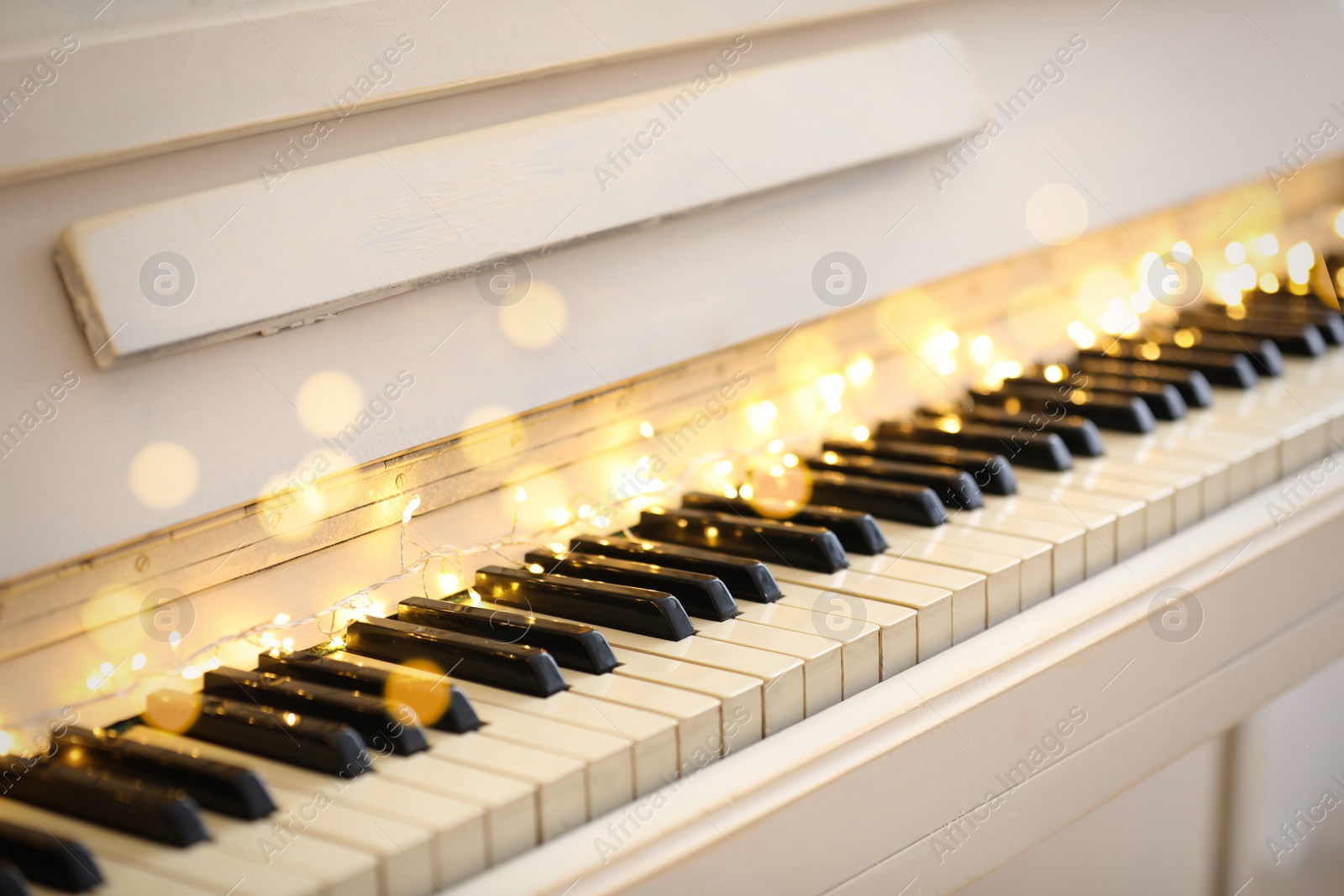 Photo of Glowing fairy lights on piano keys, closeup. Christmas music