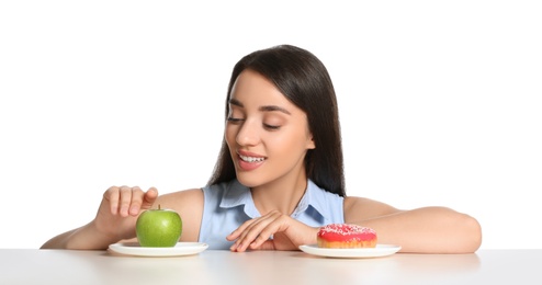 Photo of Woman choosing between apple and doughnut at table on white background