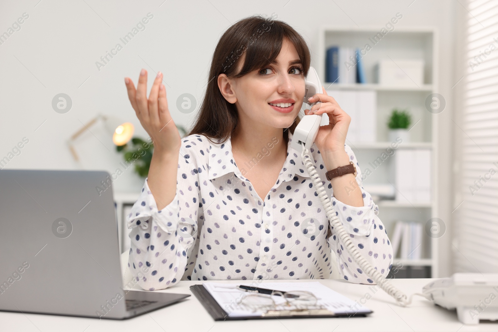 Photo of Smiling secretary talking on telephone at table in office