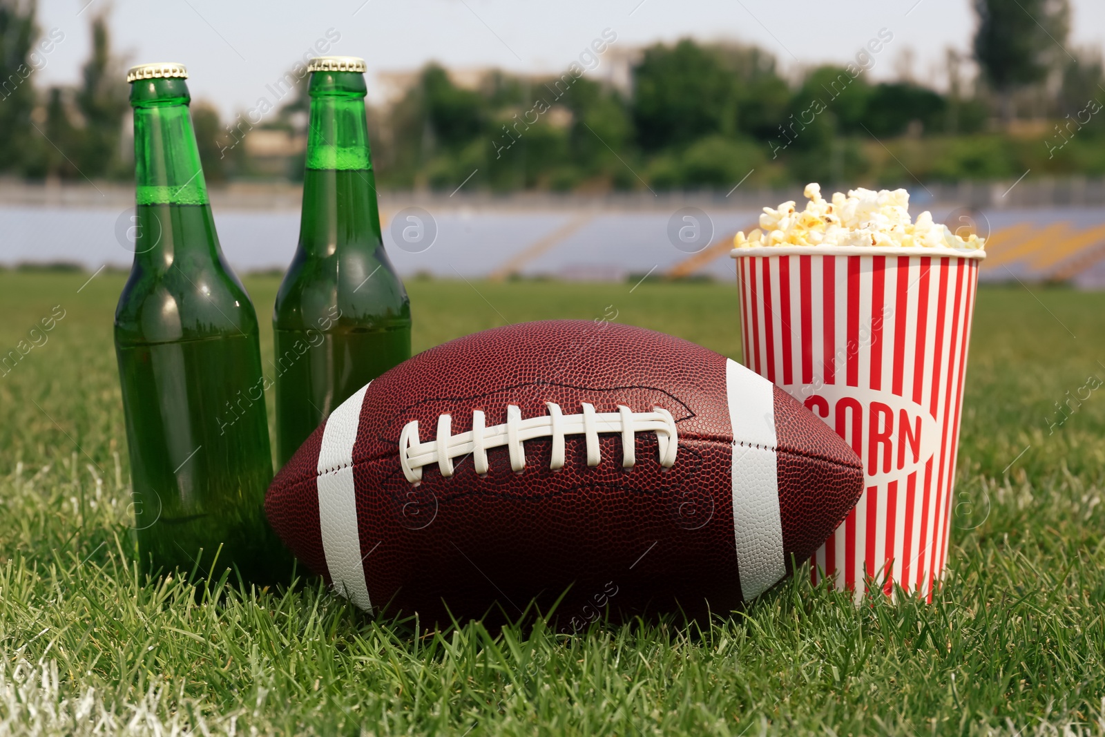 Photo of American football ball with beer and popcorn on green field grass in stadium