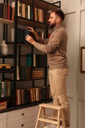 Young man choosing book on shelf in home library