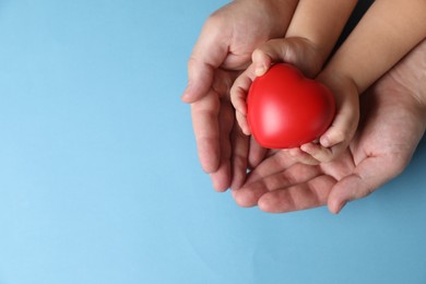 Father and his child holding red decorative heart on light blue background, top view. Space for text