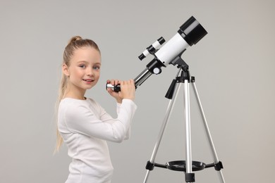 Photo of Happy little girl with telescope on light grey background