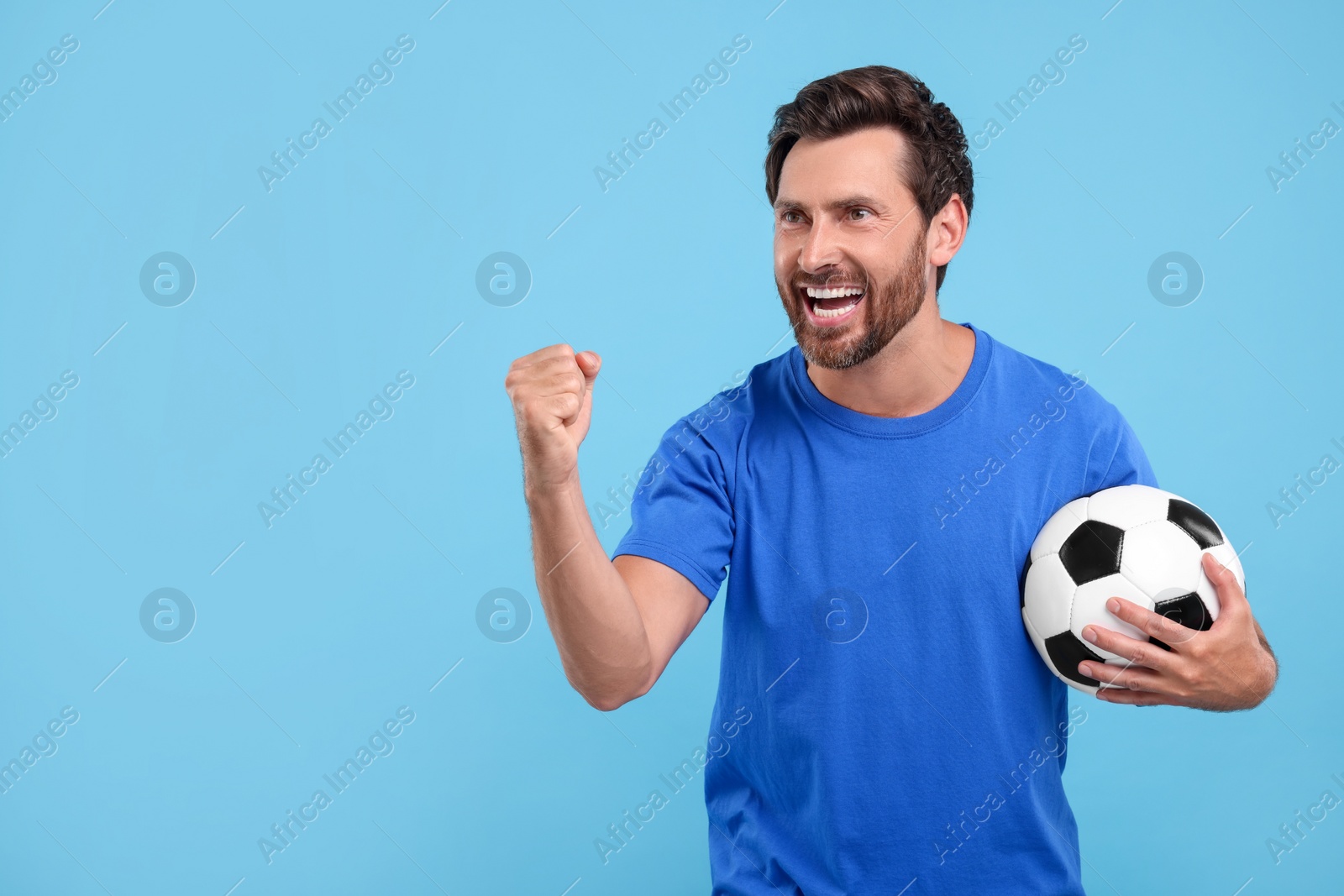 Photo of Emotional sports fan with soccer ball on light blue background, space for text