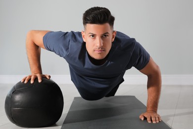 Athletic man doing push ups with medicine ball in modern gym