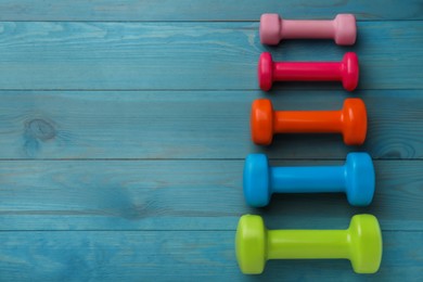 Photo of Different dumbbells on light blue wooden table, flat lay. Space for text