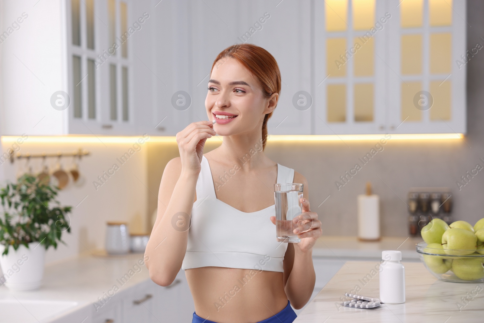 Photo of Young woman with glass of water taking pill in kitchen. Weight loss