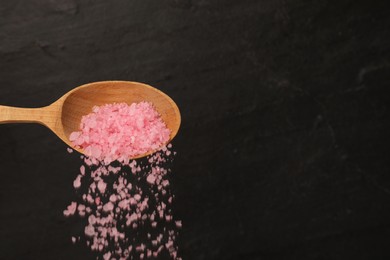 Photo of Pouring pink sea salt from wooden spoon against black background, closeup. Space for text