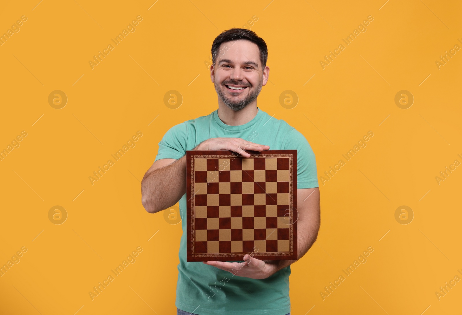 Photo of Smiling man holding chessboard on orange background