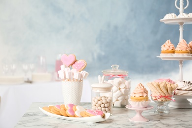 Candy bar with different sweets on white marble table against color background