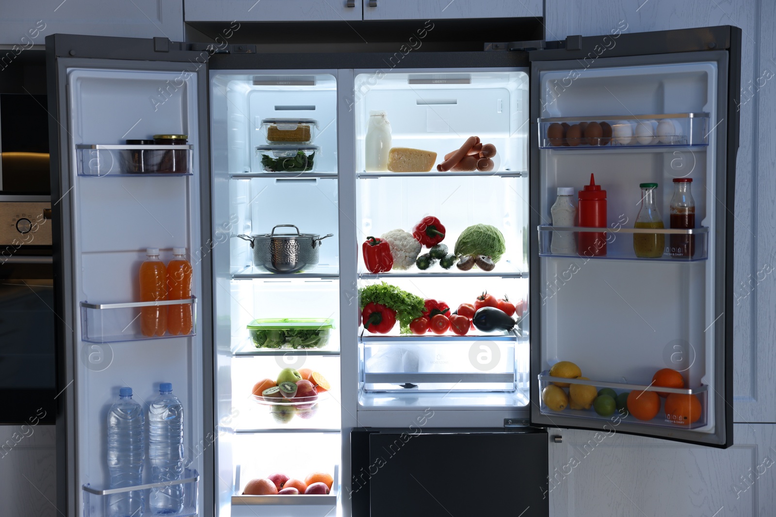 Photo of Open refrigerator full of different products in kitchen