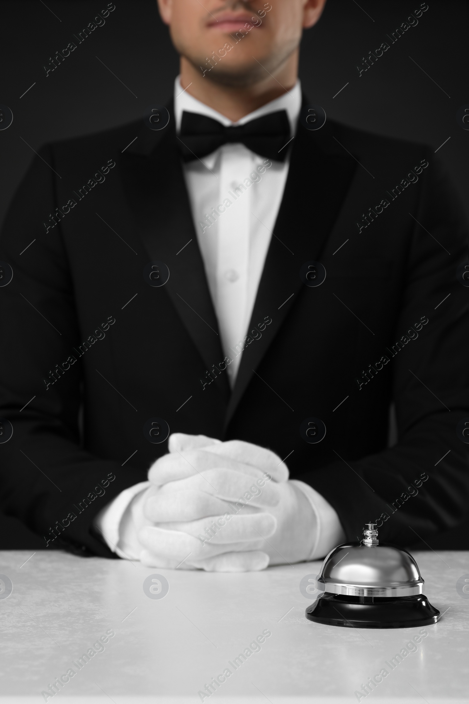 Photo of Butler at desk with service bell against black background, closeup view