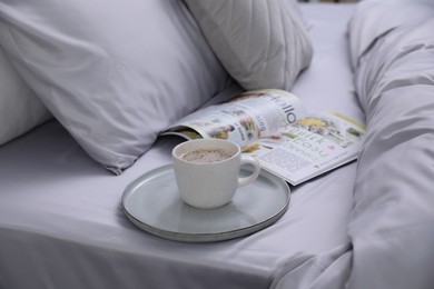 Photo of Cup of coffee and magazine on bed with soft silky bedclothes