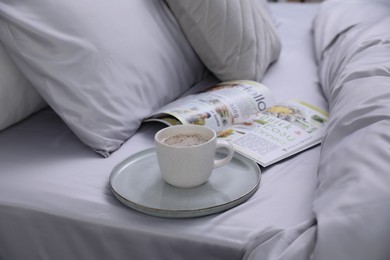 Cup of coffee and magazine on bed with soft silky bedclothes