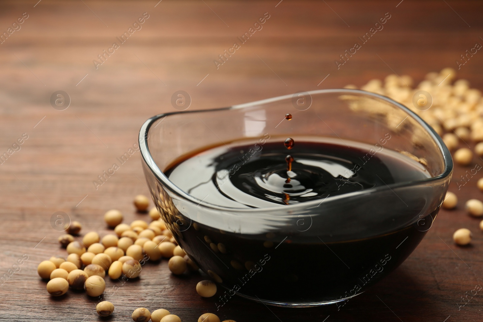 Photo of Soy sauce drops falling into bowl on wooden table, closeup