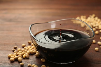 Photo of Soy sauce drops falling into bowl on wooden table, closeup