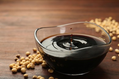 Soy sauce drops falling into bowl on wooden table, closeup