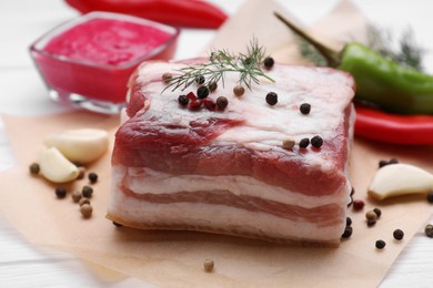 Photo of Piece of tasty pork fatback with peppercorns and garlic on white table, closeup