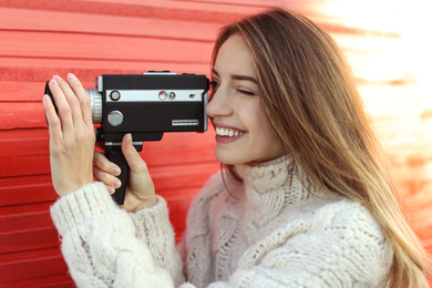 Photo of Young woman with vintage video camera near red wooden wall
