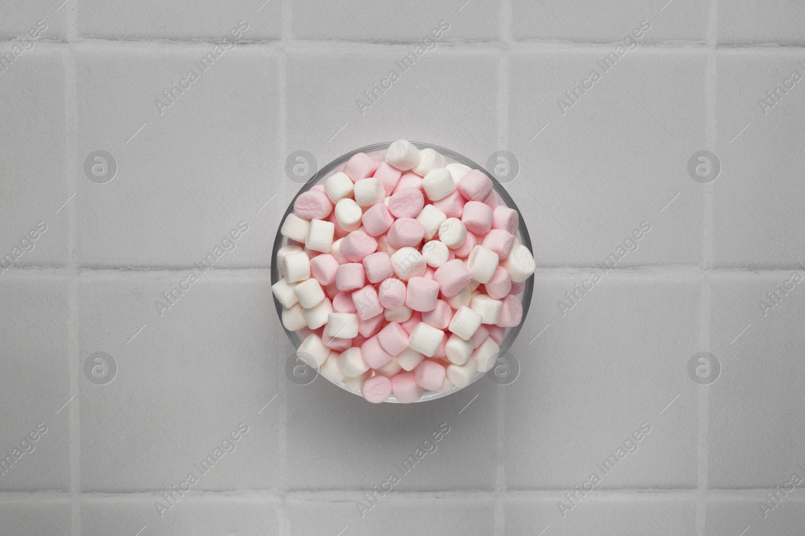 Photo of Bowl with delicious marshmallows on white tiled table, top view