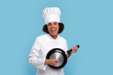 Photo of Happy female chef with frying pan having fun on light blue background