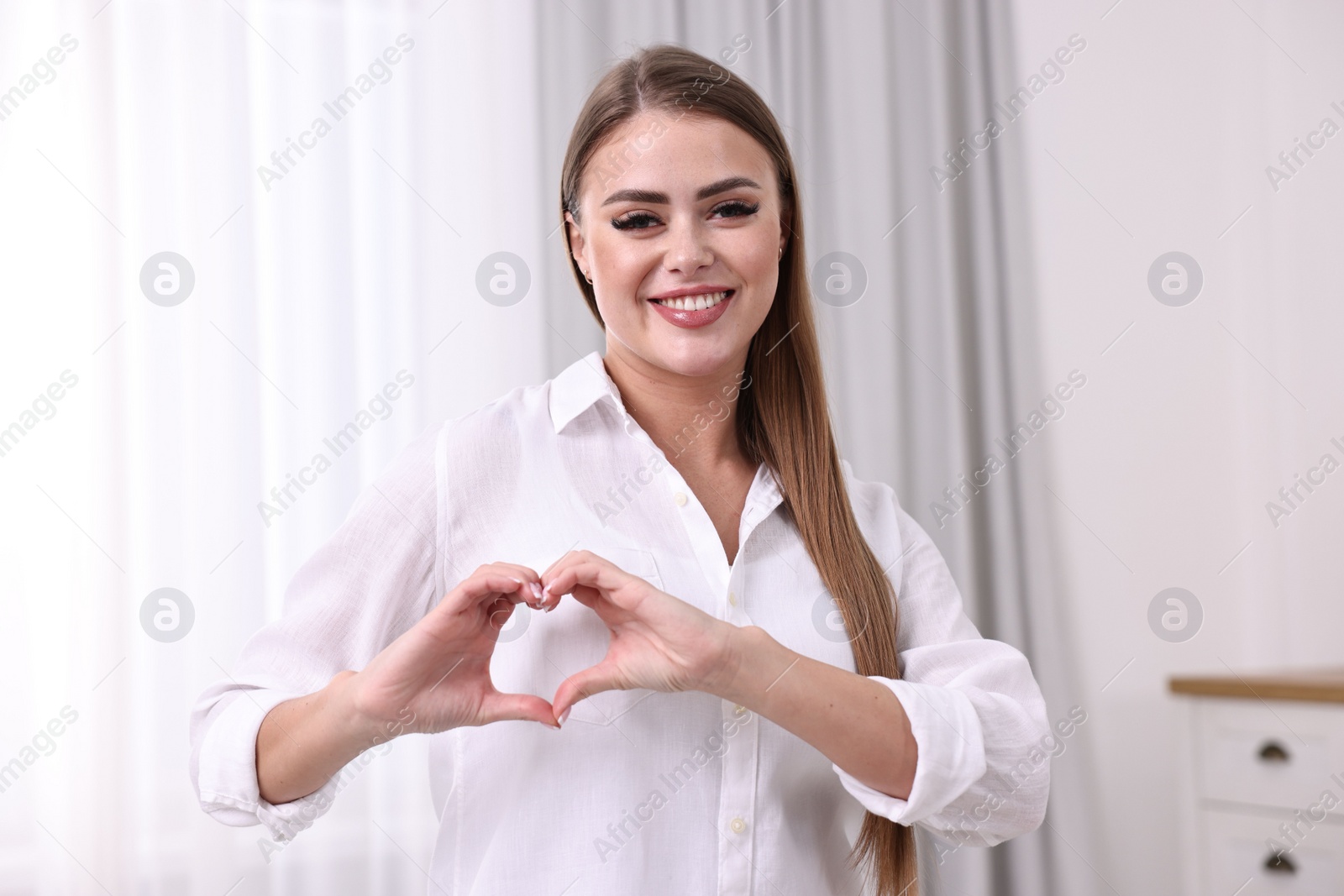 Photo of Happy woman showing heart gesture with hands indoors