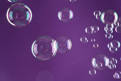 Photo of Beautiful transparent soap bubbles on purple background