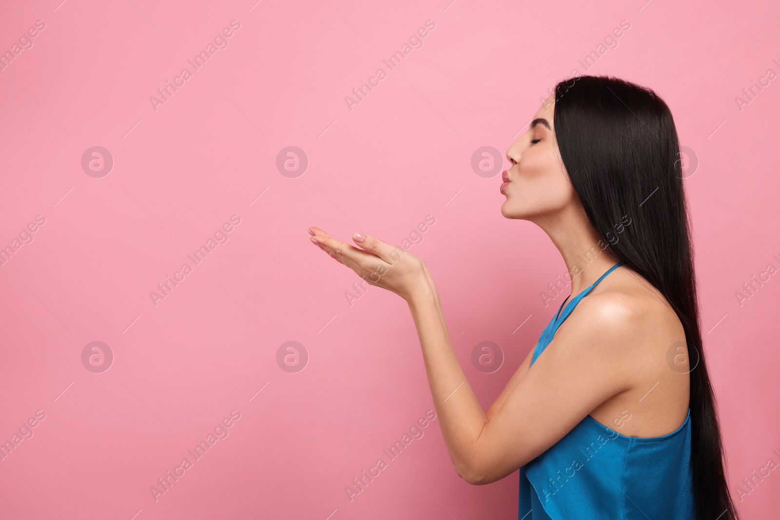 Photo of Beautiful young woman blowing kiss on pink background. Space for text