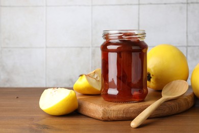 Photo of Tasty homemade quince jam in jar, spoon and fruits on wooden table. Space for text