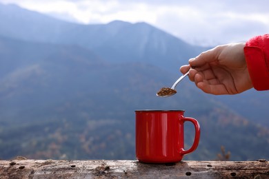 Photo of Woman pouring instant coffee into mug in mountains, closeup. Space for text