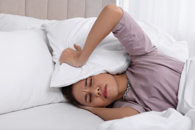Unhappy African American woman covering ears with pillows in bed at home