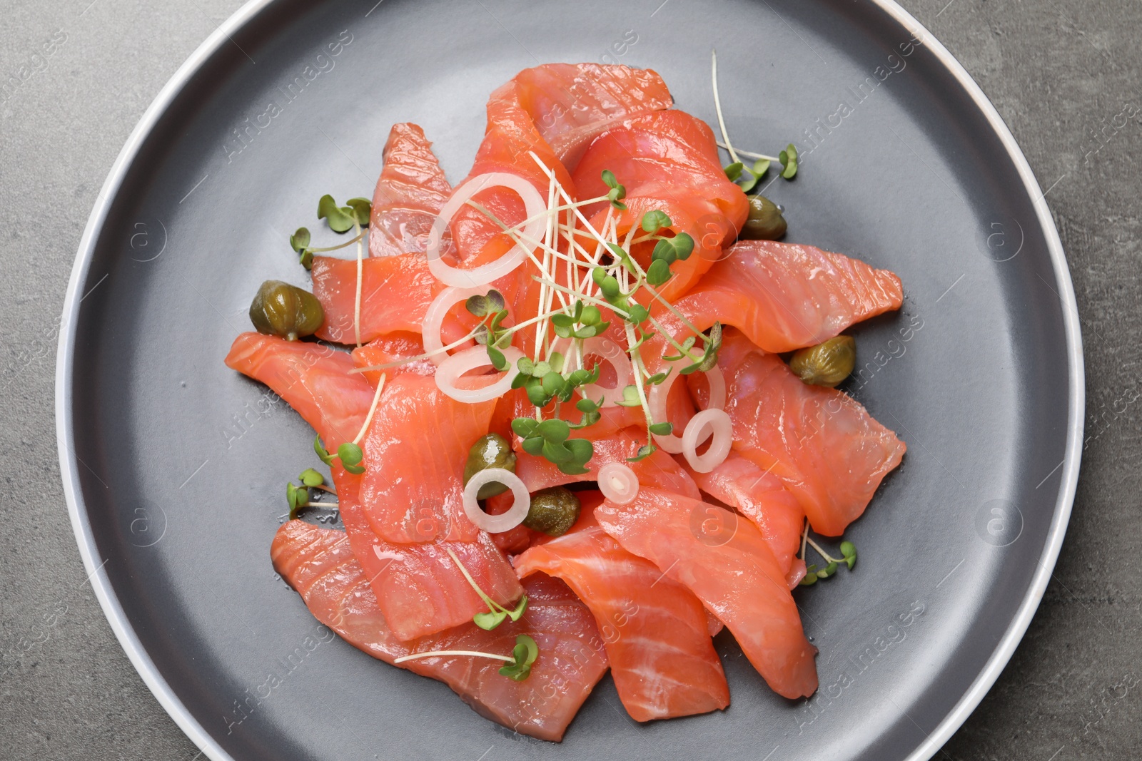 Photo of Salmon carpaccio with capers, onion and microgreens on grey table, top view