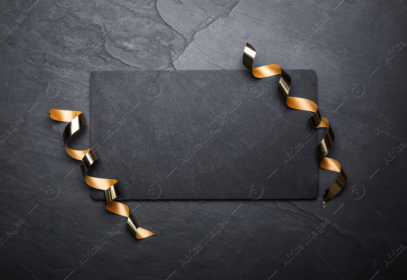 Photo of Slate board and serpentine streamers on black background, top view. Space for text