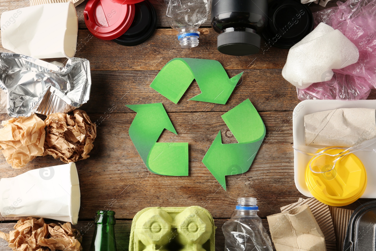 Photo of Recycling symbol and different garbage on wooden background, top view