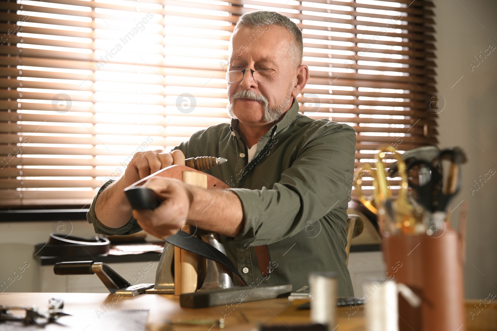 Photo of Man burnishing edges of leather belt in workshop